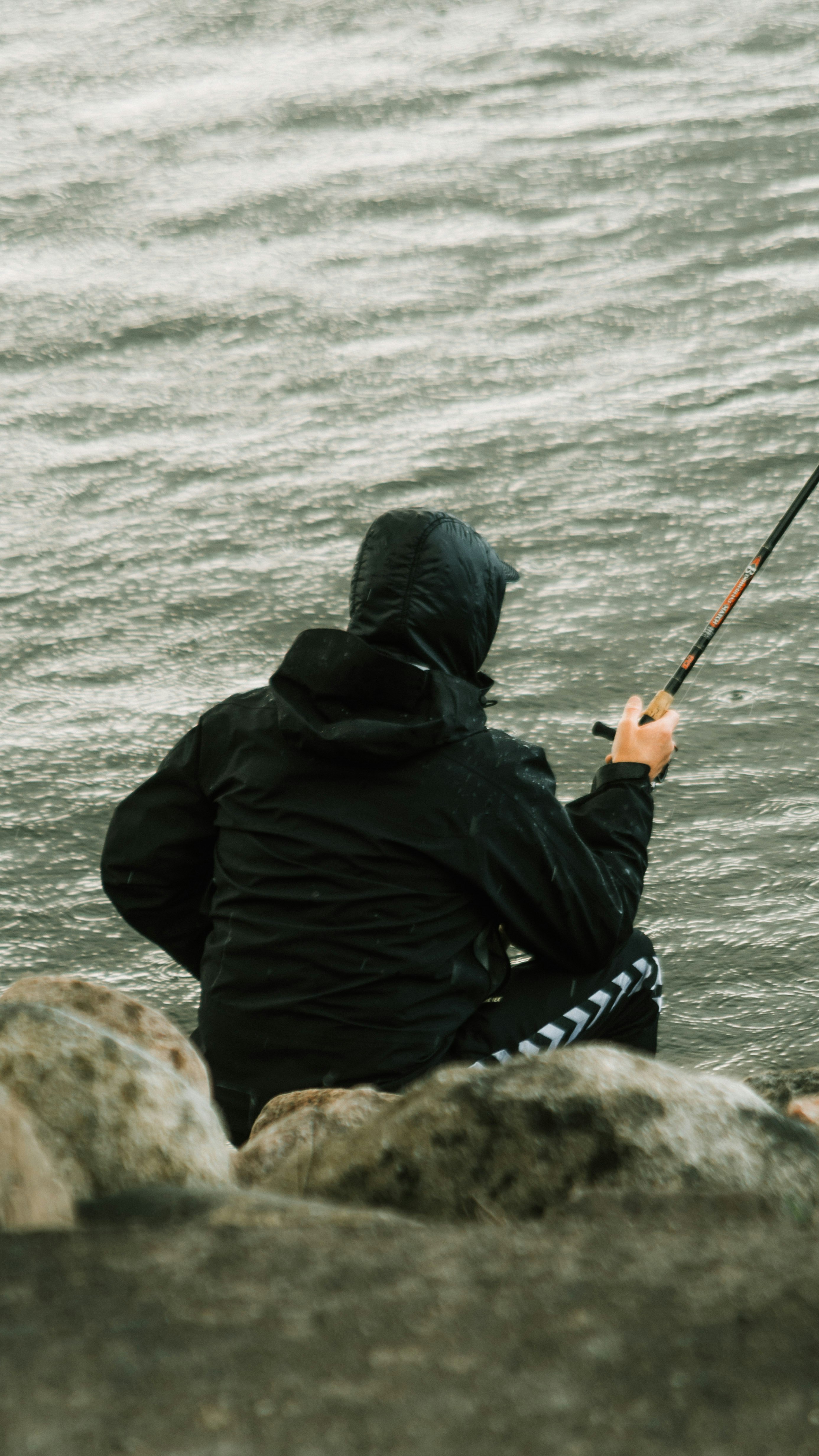 person in black jacket fishing on sea during daytime